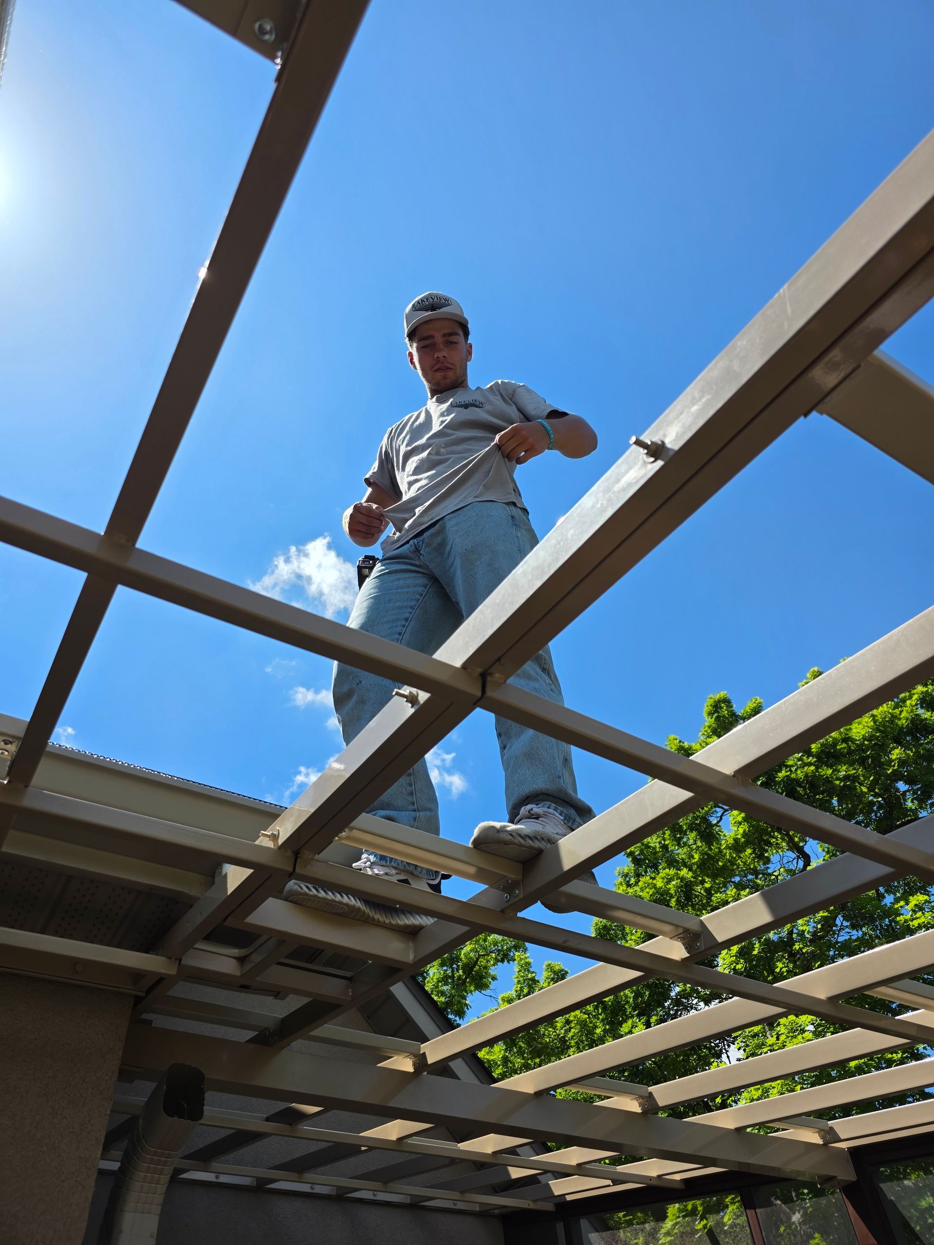 Worker standing on roof beams under blue sky, inspecting a wooden structure on a construction site