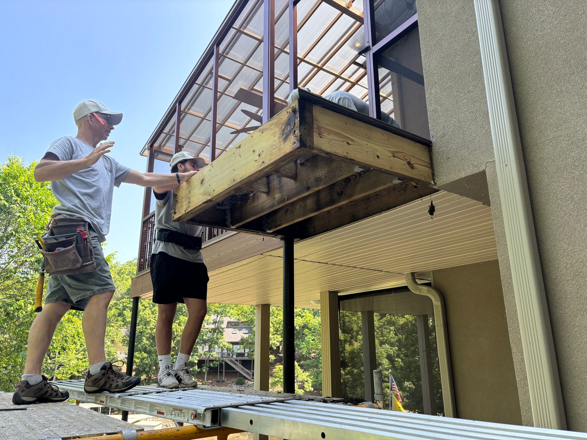 Two workers installing a balcony deck on the side of a house