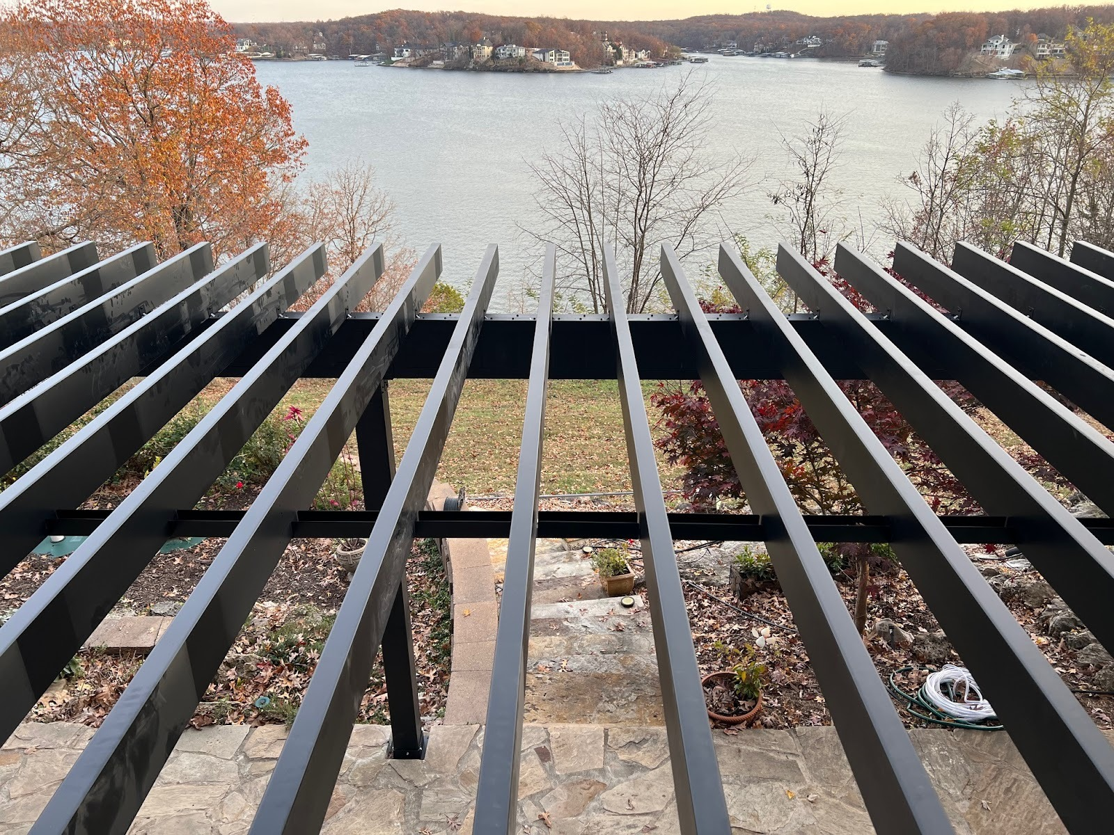White railing and steps leading up from a gravel path, next to a concrete wall and wooded area.