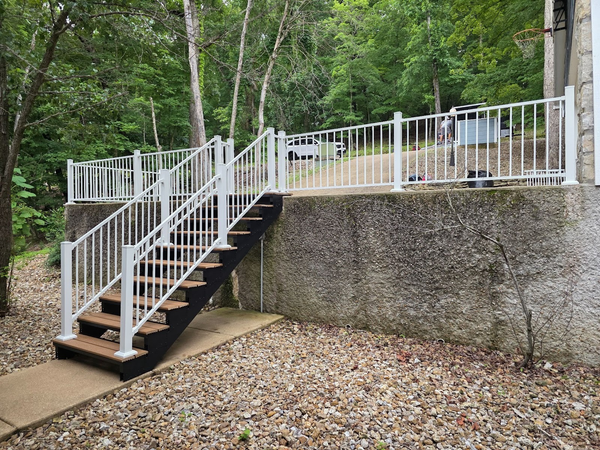 Black pergola over a white house, built into a concrete retaining wall, surrounded by trees.