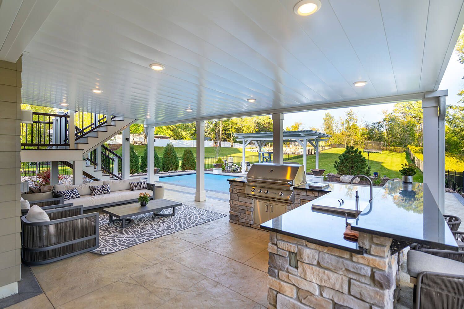 Deck with black railing, pool, and lakeside view surrounded by trees and lush greenery.