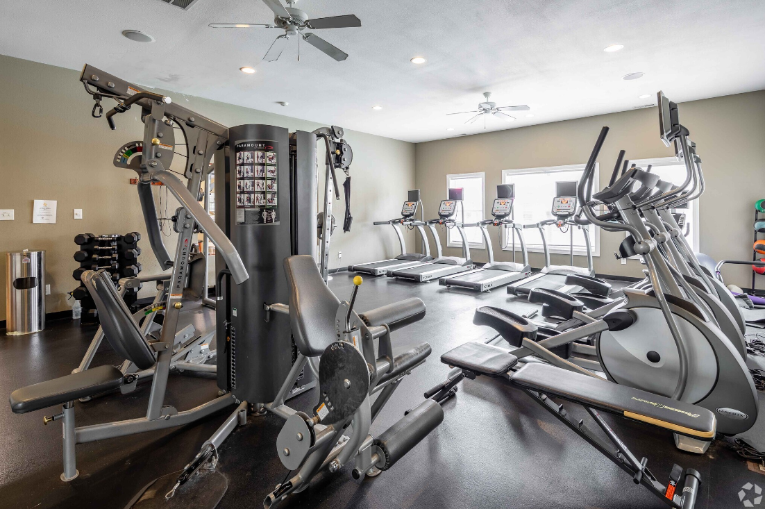 A large gym filled with lots of exercise equipment and a ceiling fan.