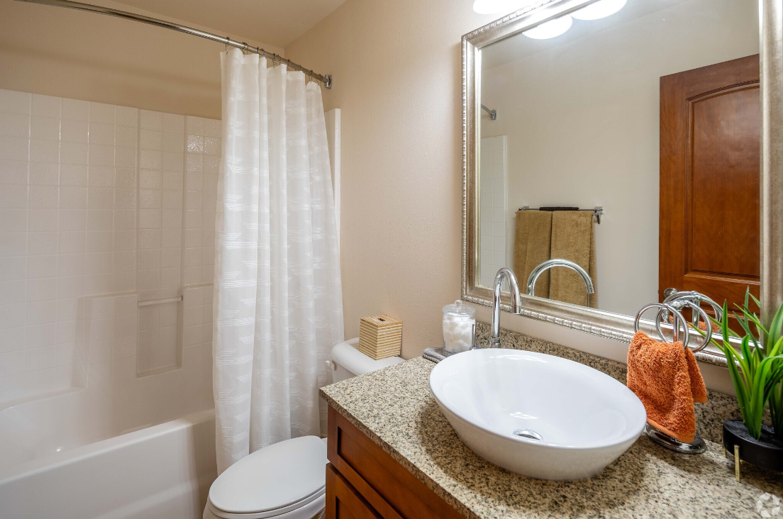 A bathroom with a sink , toilet , shower and mirror.