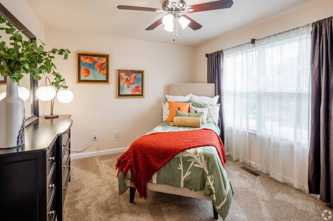 A bedroom with a bed , dresser , mirror and ceiling fan.