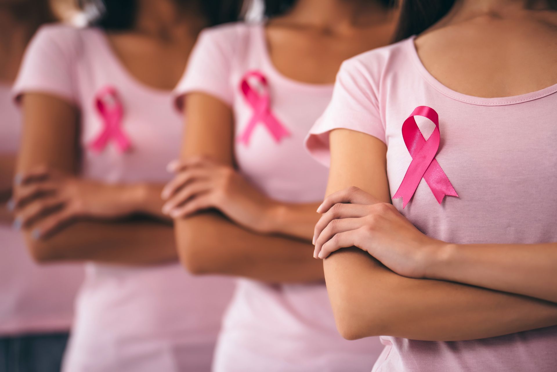 Women in pink shirts with pink ribbons, arms crossed, representing breast cancer awareness.