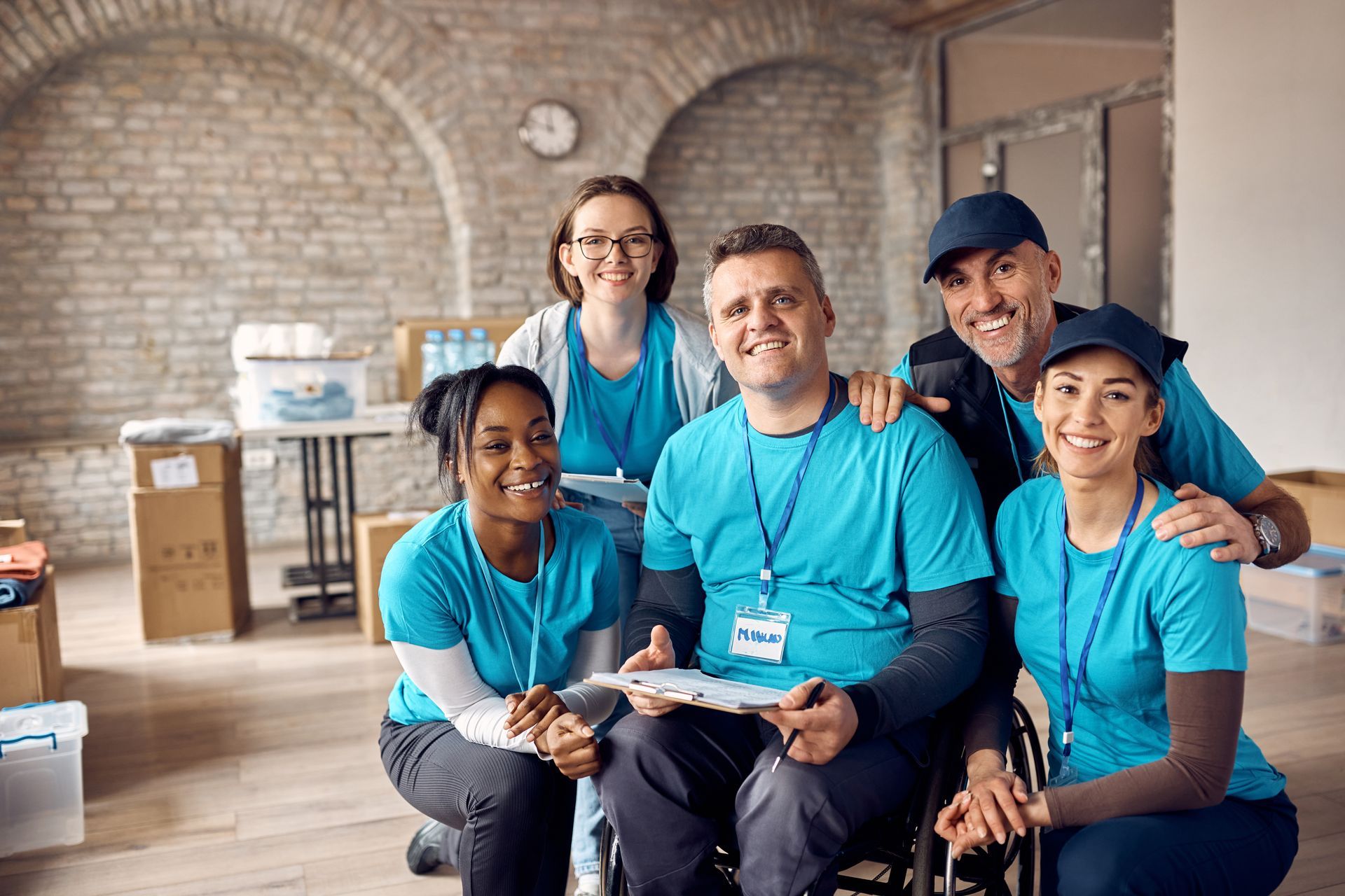Smiling group of volunteers wearing blue shirts posing, with a person in a wheelchair.
