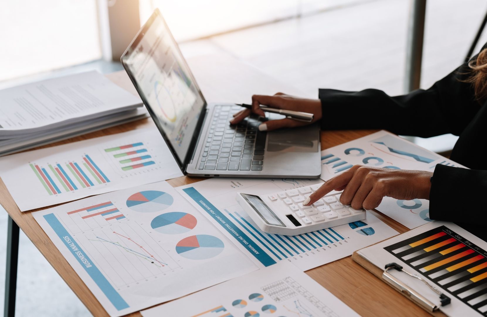 A woman is sitting at a desk using a laptop and a calculator.