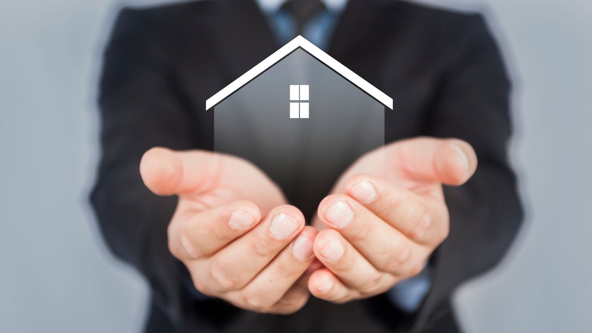 A man in a suit is holding a small house in his hands.