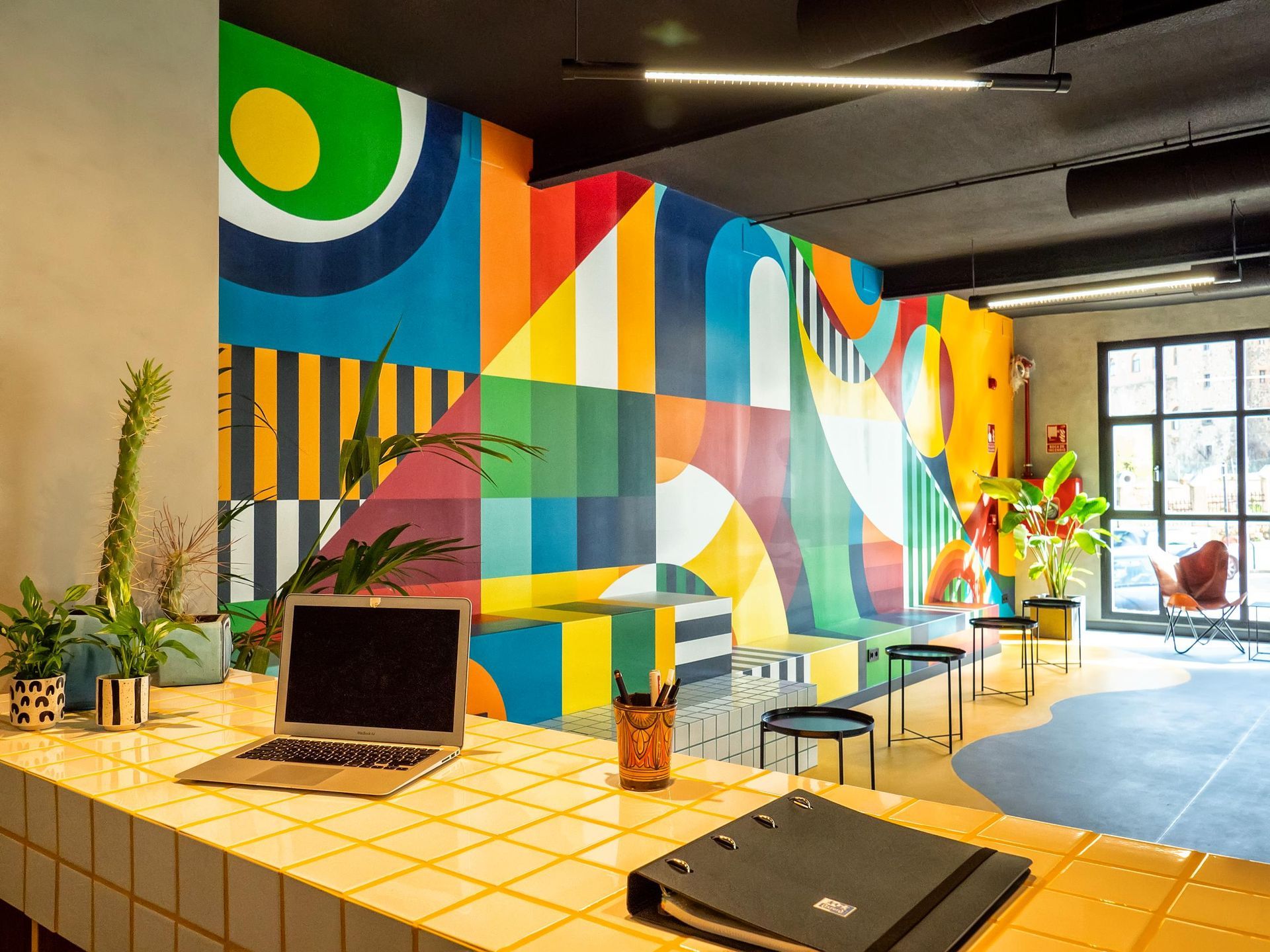 A laptop computer is sitting on a counter in front of a colorful wall mural.