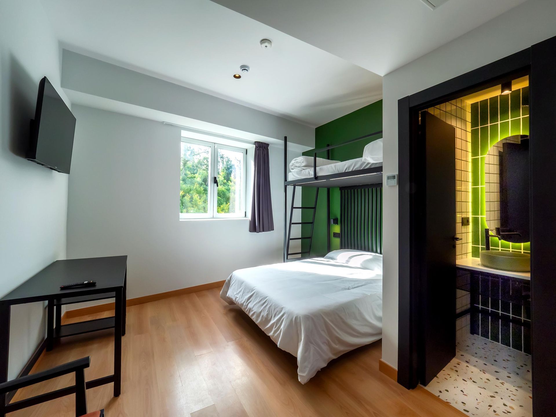 A hotel room with a bunk bed , desk , television and bathroom.