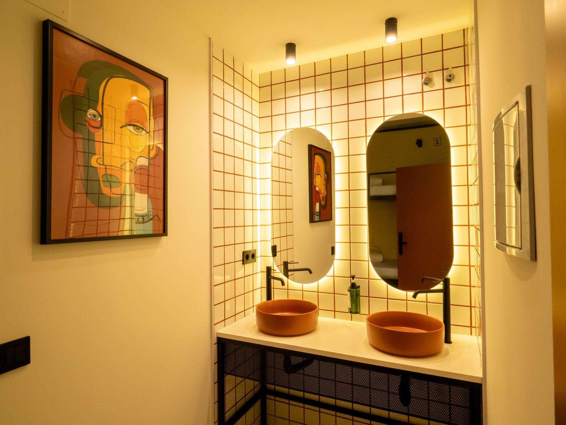 A bathroom with two sinks , two mirrors and a painting on the wall.
