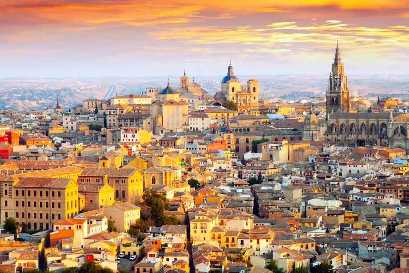 An aerial view of a city at sunset with a cathedral in the background.