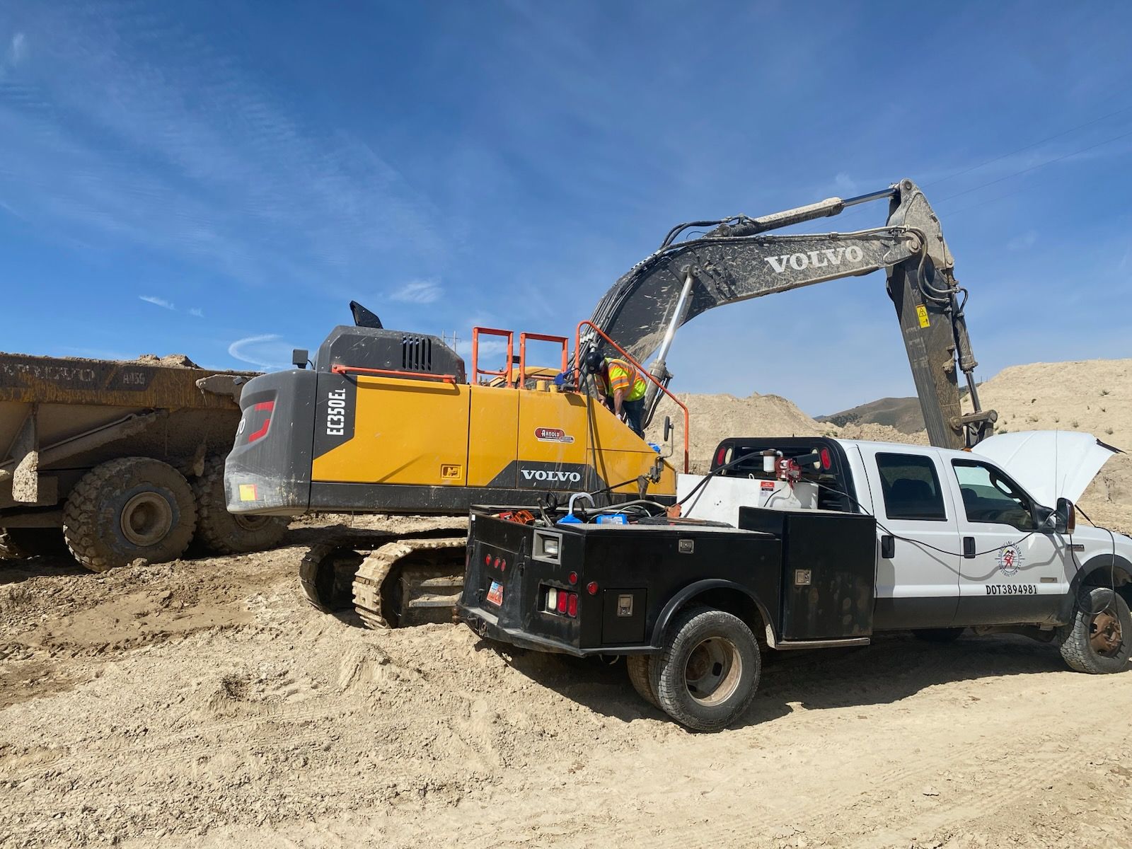 A truck is towing a large excavator in a dirt field.