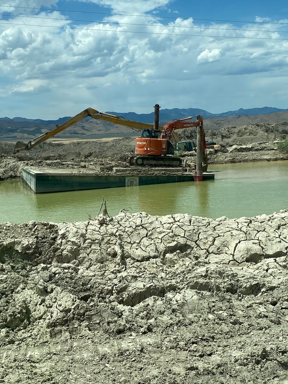 A large excavator is sitting on a raft in the middle of a body of water.