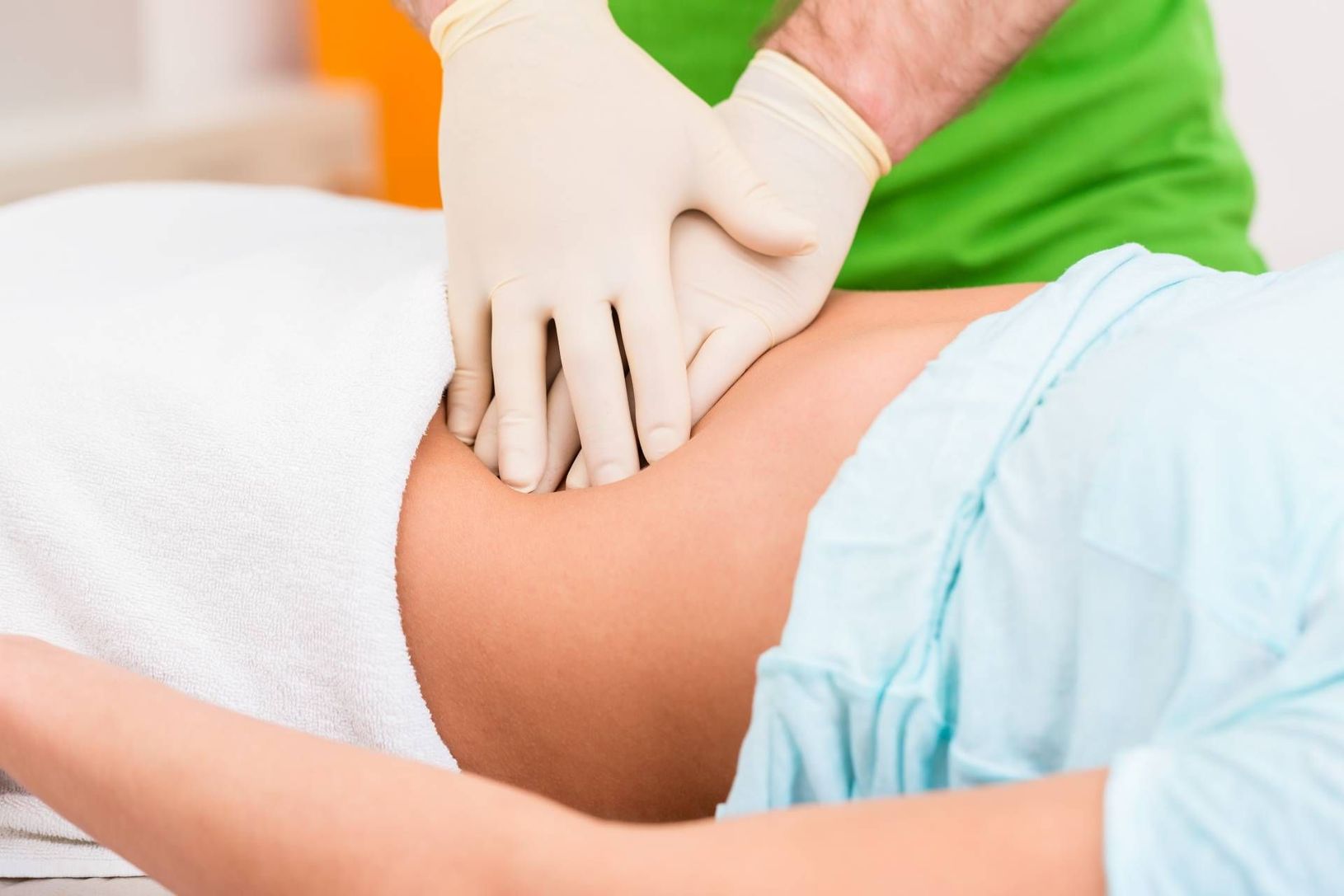Healthcare worker wearing gloves giving abdominal massage to a patient on a table