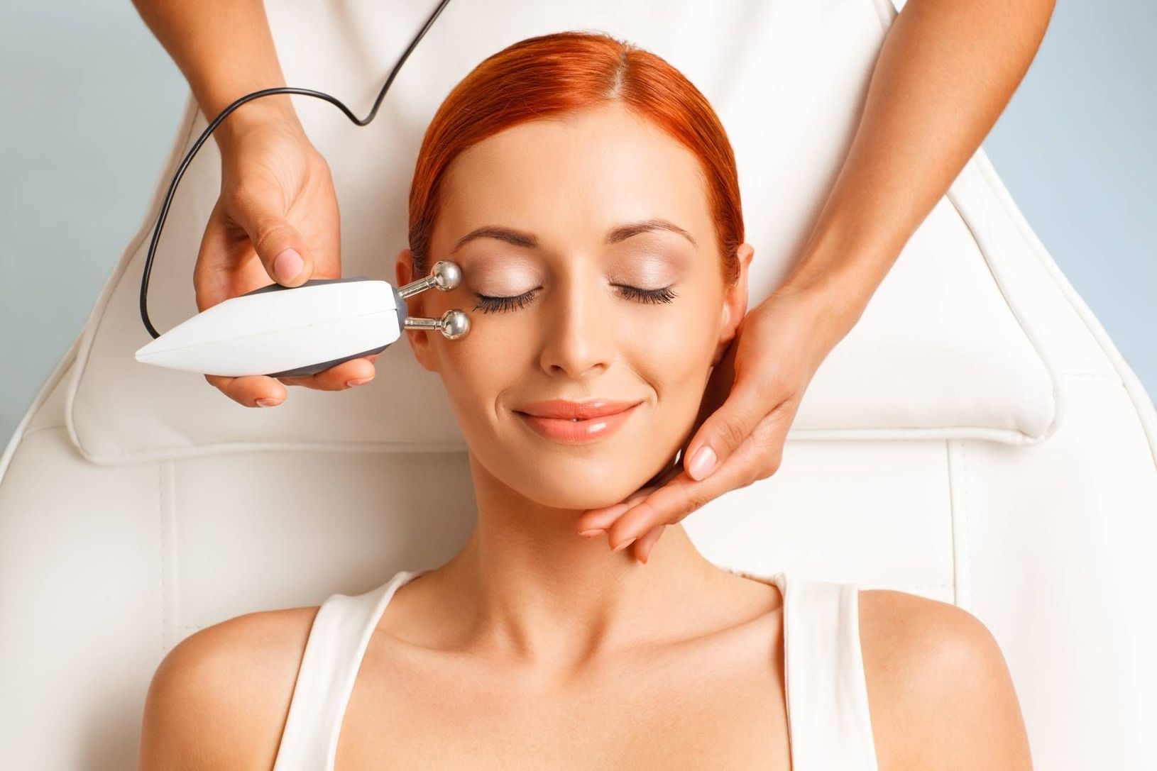 Woman receiving a facial treatment with a handheld device and massage on a spa bed