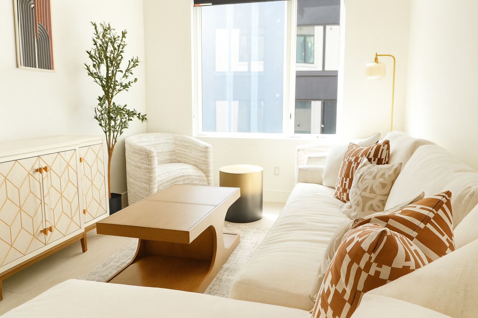 A cozy living room with a white sectional sofa, patterned pillows, a light-wood coffee table, and a textured accent chair.