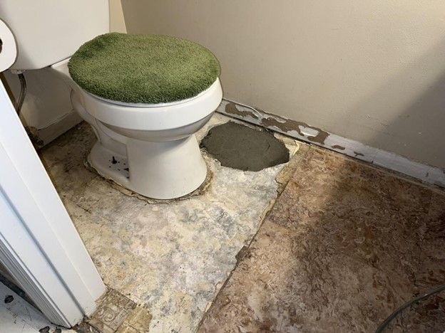 A toilet with a green seat cover is sitting on a tiled floor in a bathroom.