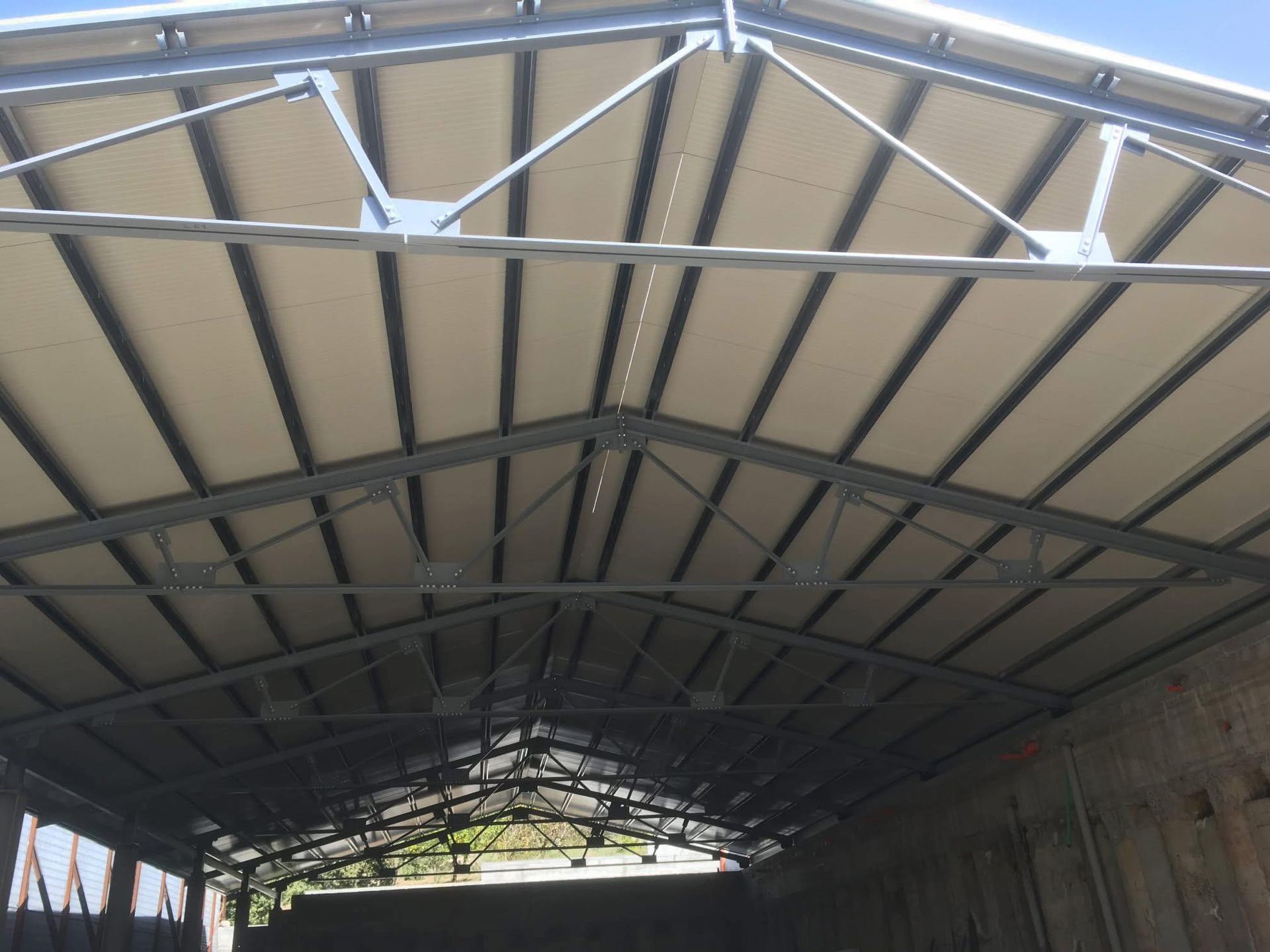 Struttura del tetto con struttura metallica e pannelli bianchi visibili dal basso. La luce del sole filtra attraverso le aperture.