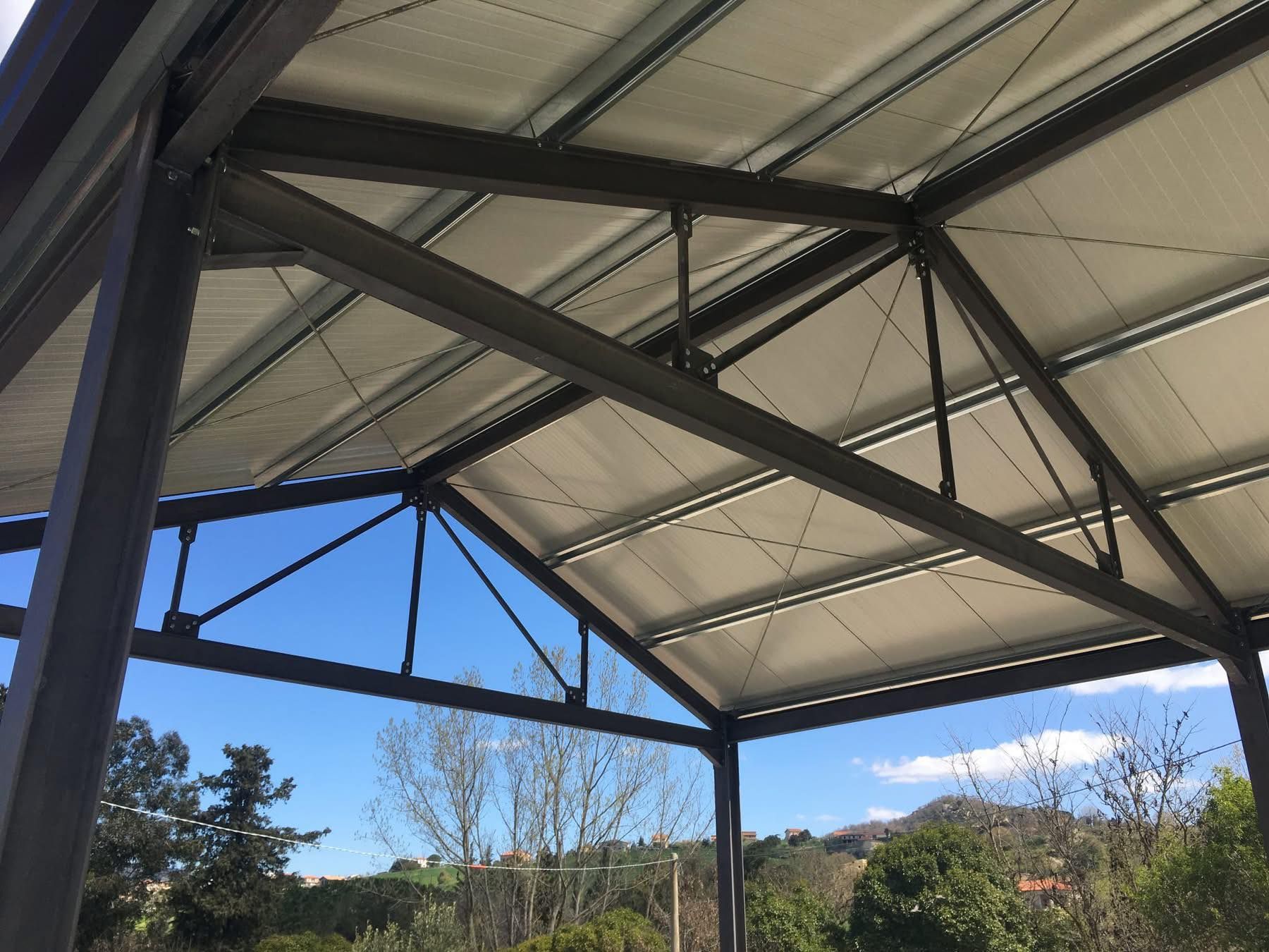 Pensilina con struttura in metallo e tetto in tessuto bianco, cielo azzurro sullo sfondo.