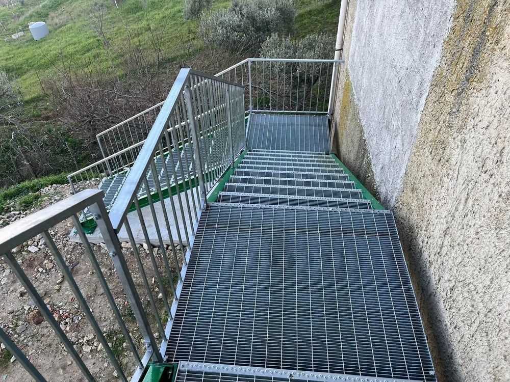 Scala metallica che scende lungo un muro di cemento e un pendio erboso.