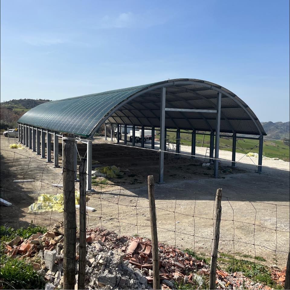 Struttura metallica con tetto ad arco, aperta sui lati, in costruzione all'aperto in una giornata di sole.