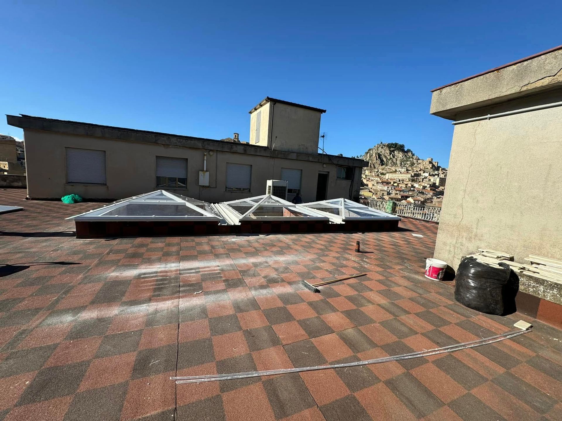 Tetto con lucernari, tegole rosse e marroni e altri edifici in lontananza sotto un cielo azzurro e terso.