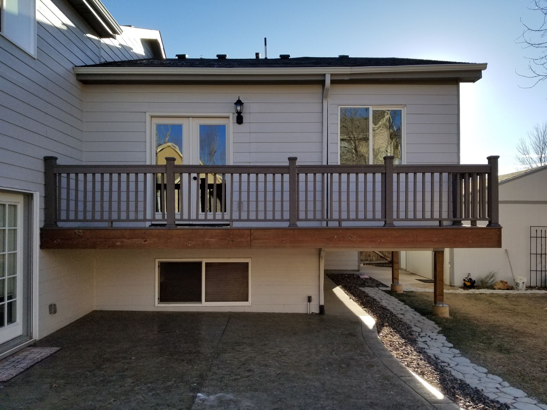 Gray house with brown deck, railing, and concrete patio.