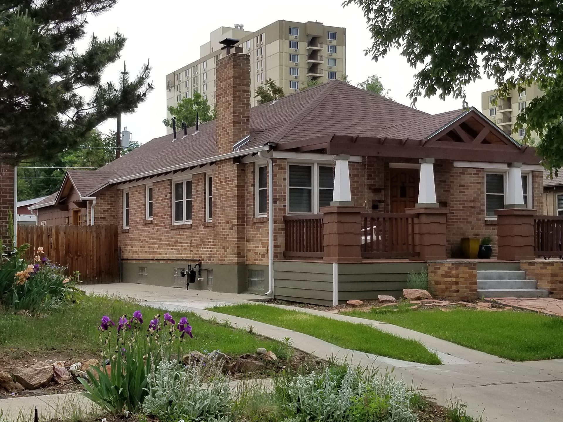 Brick house with brown roof, porch, and chimney; driveway with green lawn and flower bed in front.