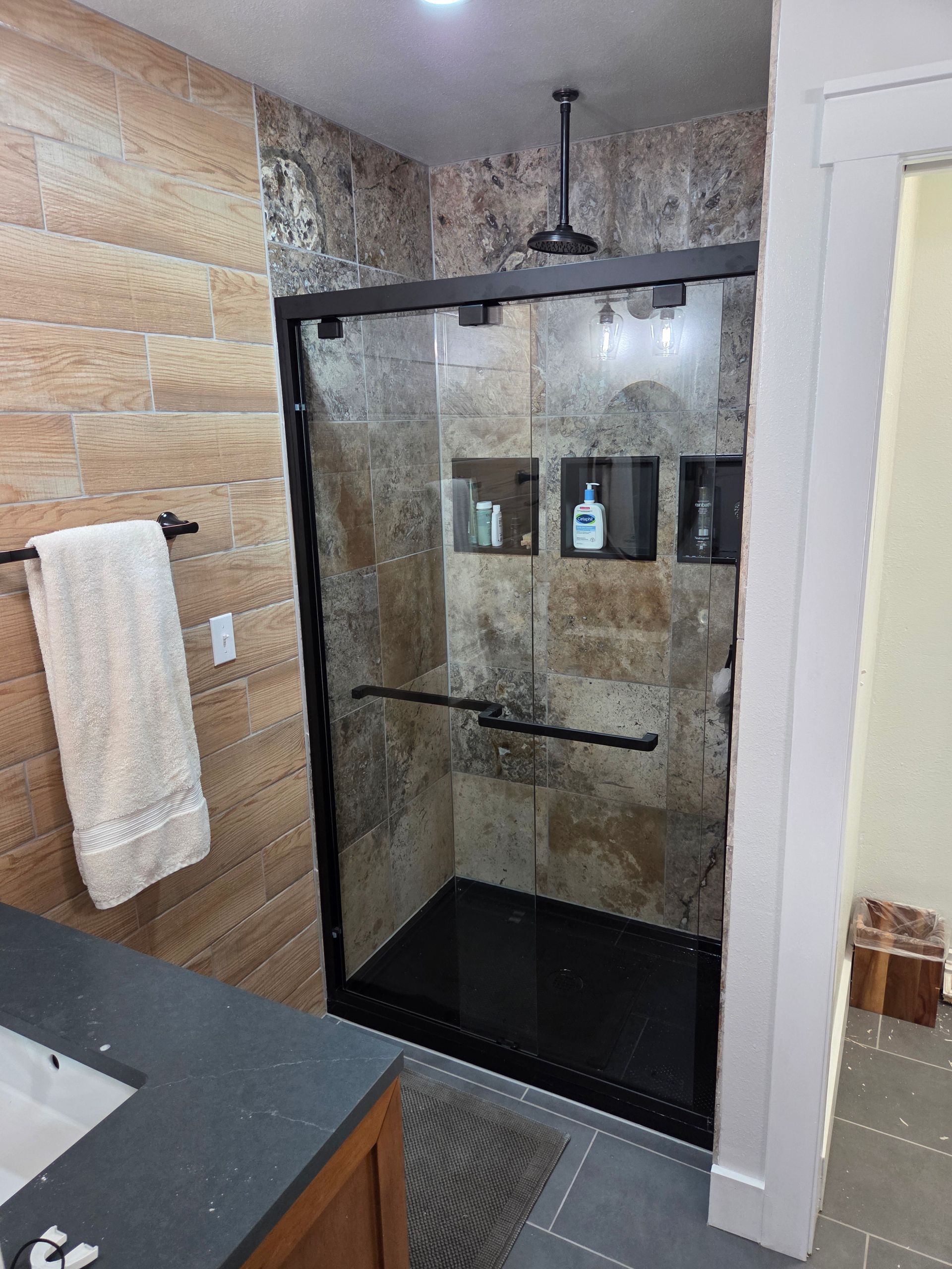 Bathroom with black-framed shower, dark floor, tile walls, recessed shelves, and a towel rack.