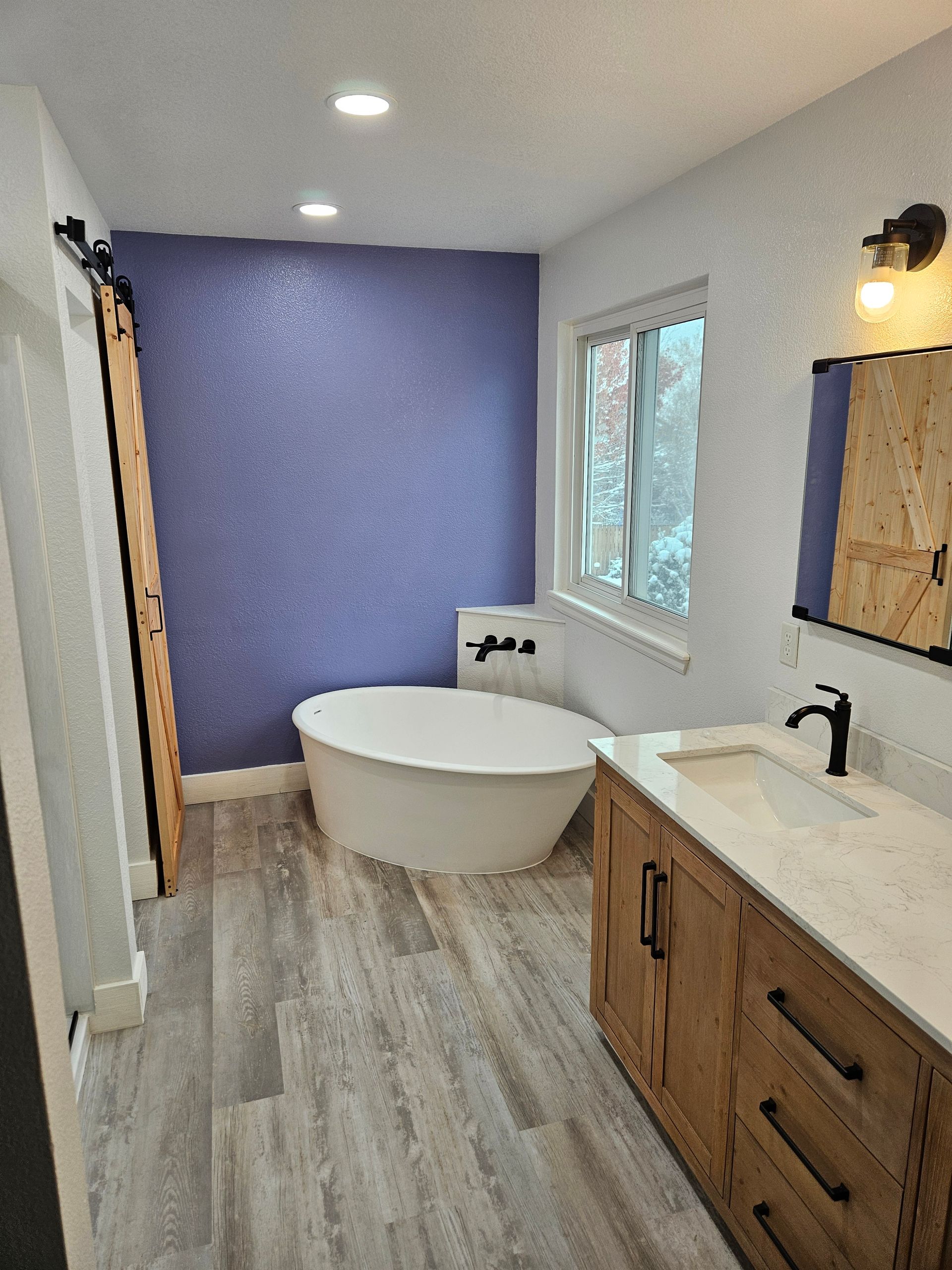 Bathroom with a blue accent wall, soaking tub, wooden vanity, and a barn door.