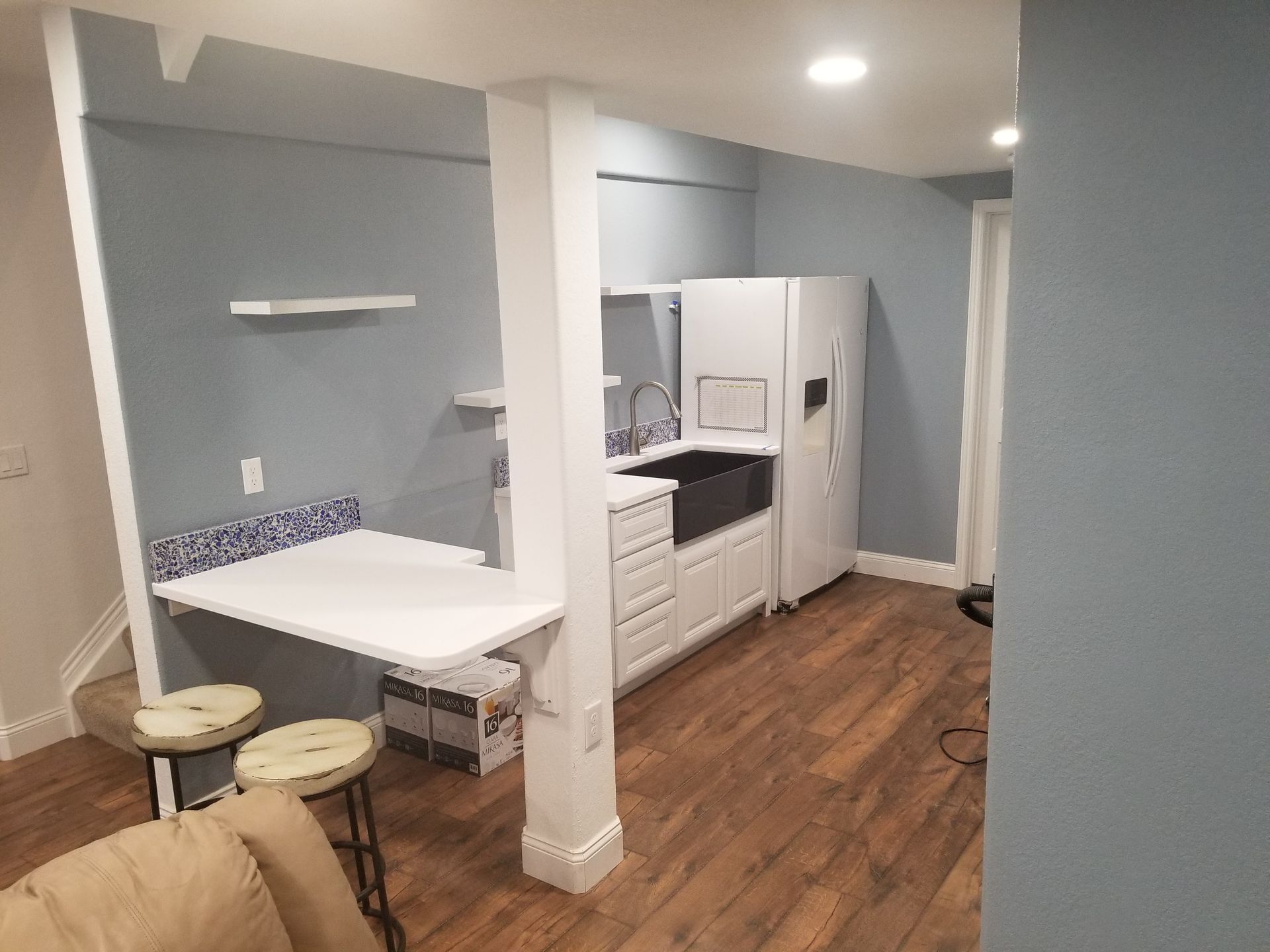 Basement kitchen with white cabinets, black sink, and fold-out table. Light blue walls, wood floors.