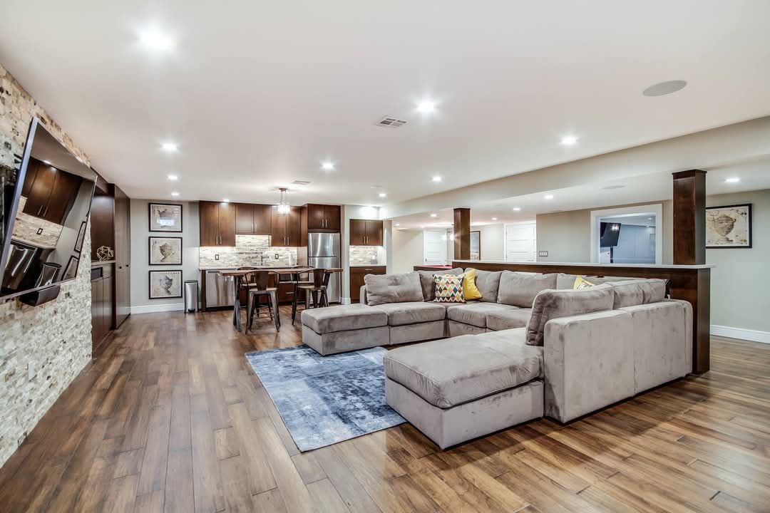 Open-concept basement with sectional sofa, kitchen, and wood flooring.