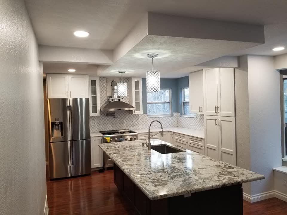 Modern kitchen with a large granite island, white cabinets, and stainless steel appliances.