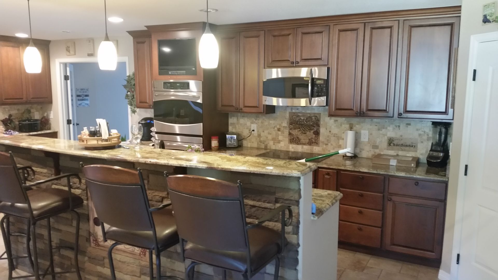 Kitchen with brown cabinets, granite countertops, and a breakfast bar with three bar stools.