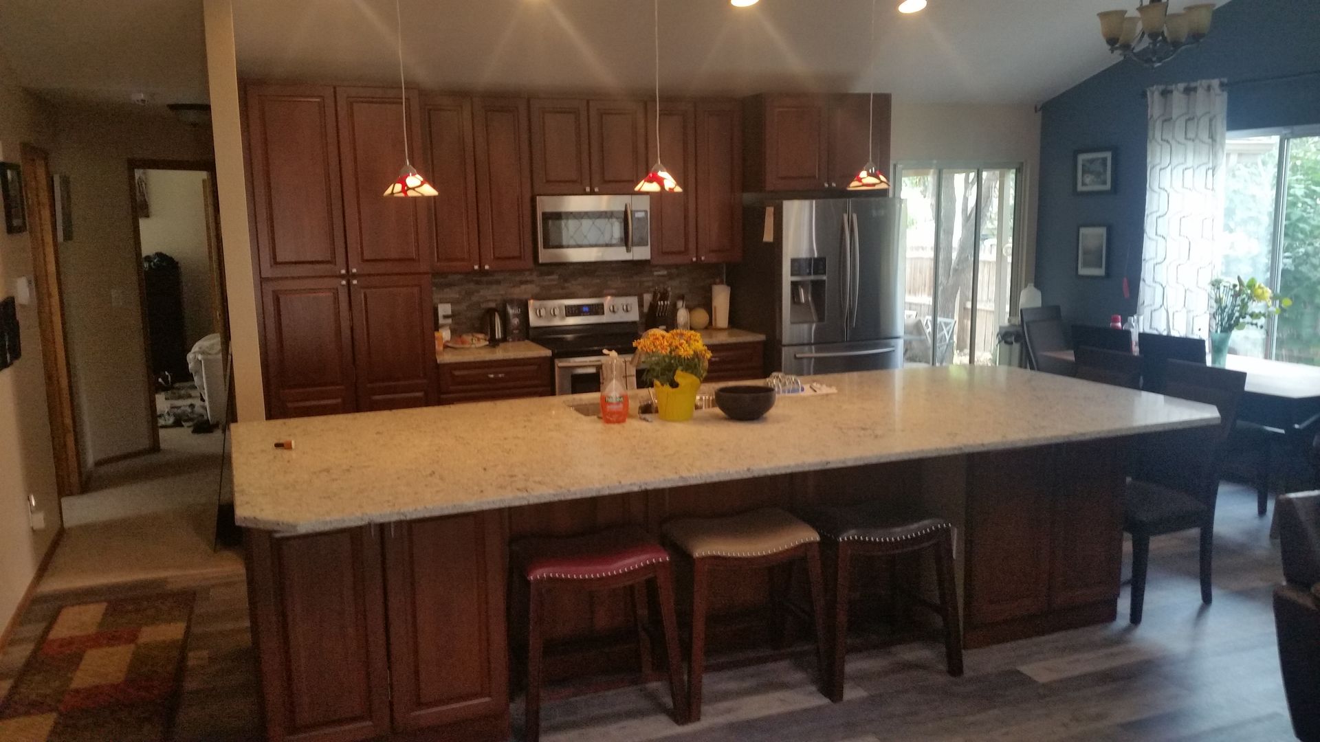 Kitchen with brown cabinets, island with stools, stainless steel appliances, and a dining area.