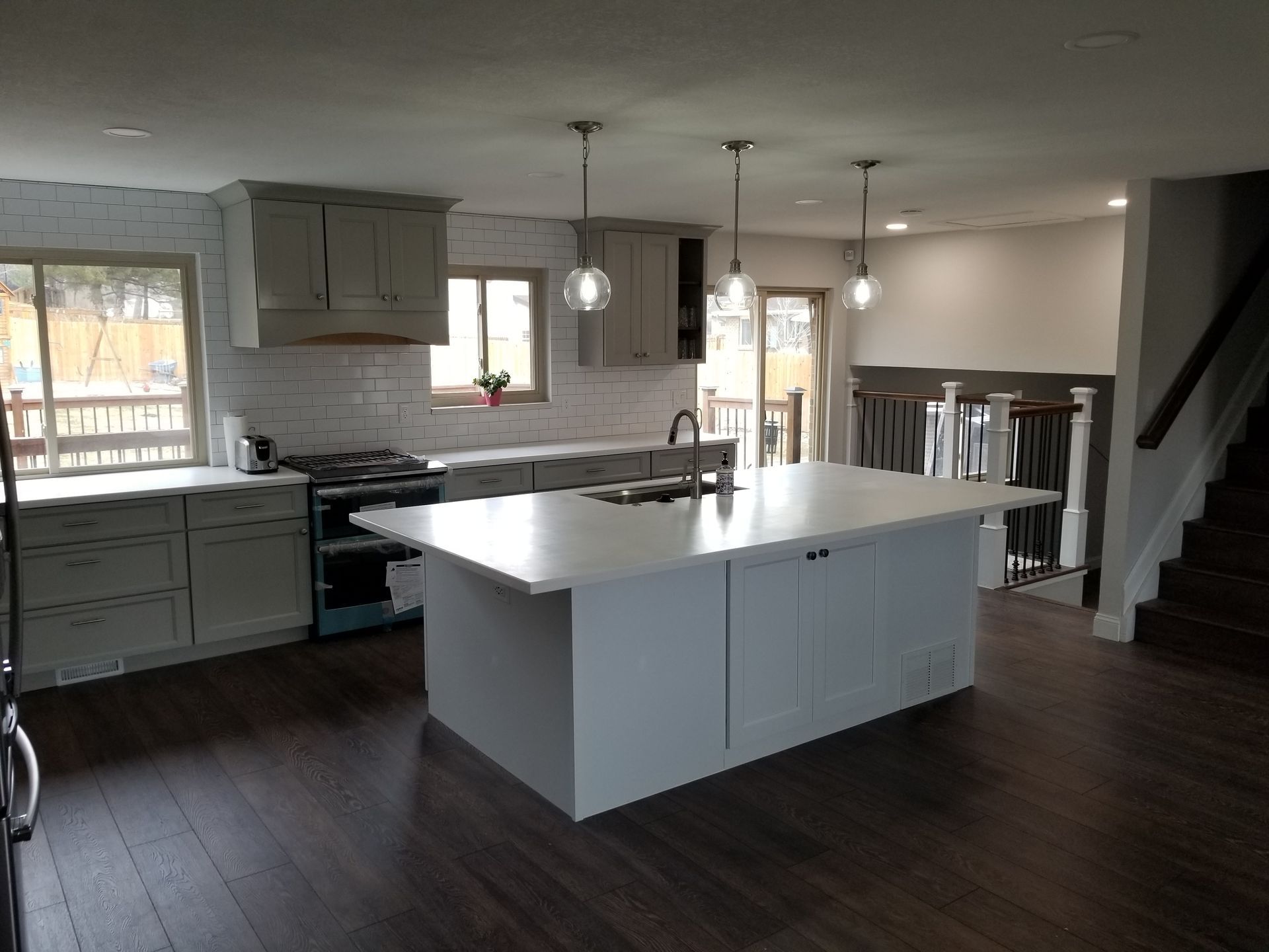 Modern kitchen with island, cabinets, and staircase. Gray and white tones. Dark wood floor.