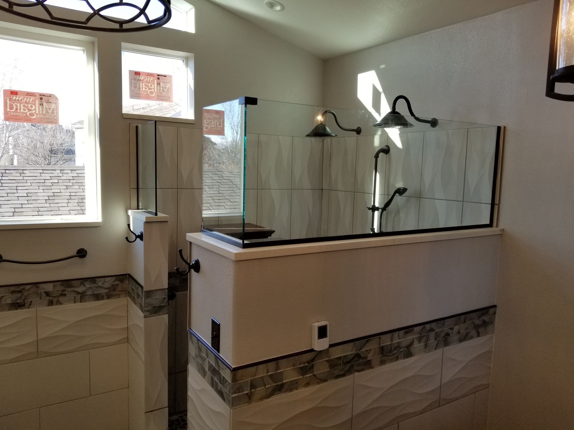 Modern bathroom with glass shower enclosure, white and patterned tile, and arched shower heads.