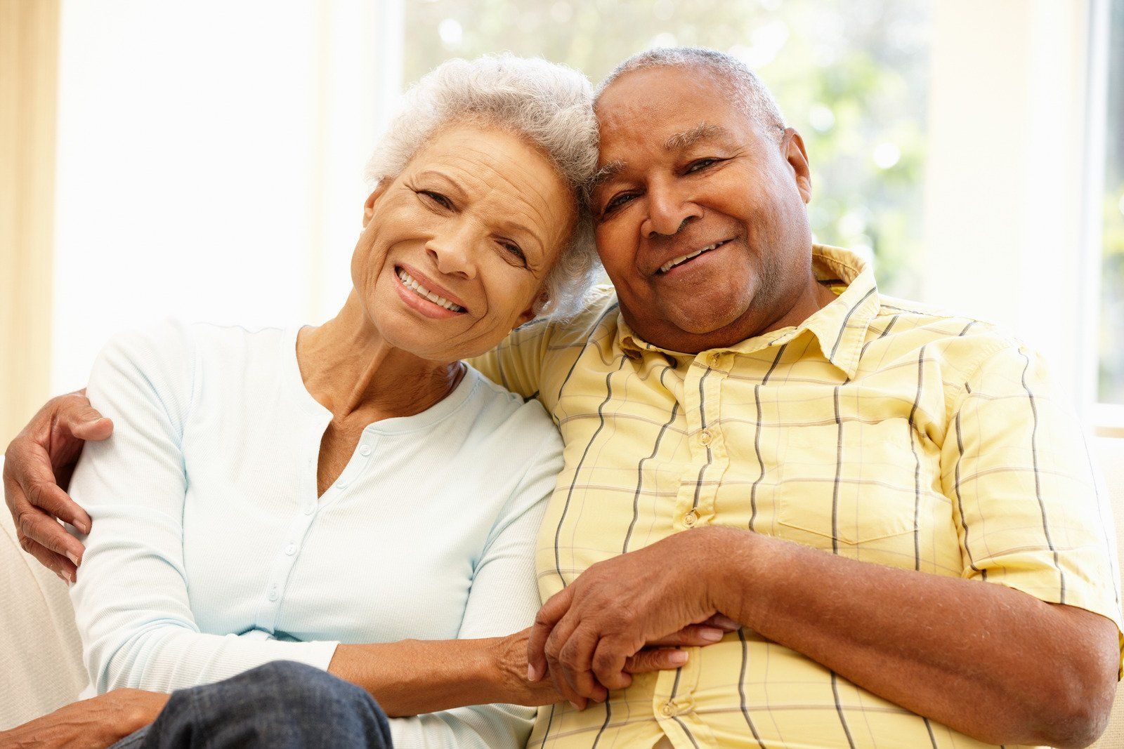 An elderly couple is sitting on a couch and hugging each other.