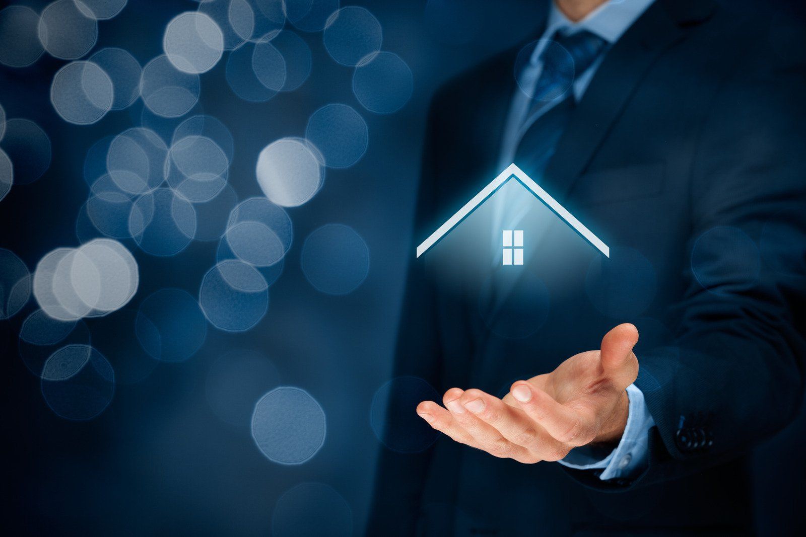 A man in a suit and tie is holding a house in his hand.