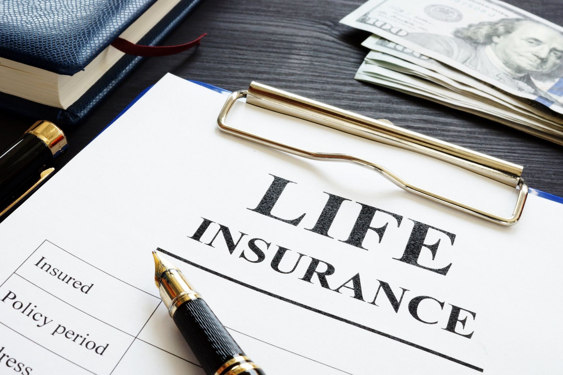 A pen is sitting on top of a clipboard that says life insurance.