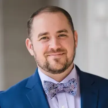 A man with a beard is wearing a blue suit and a bow tie.