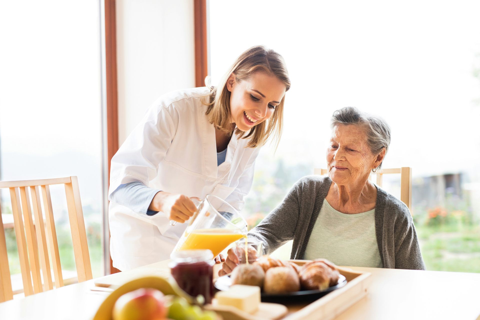 A nurse is serving an elderly woman a cup of orange juice.