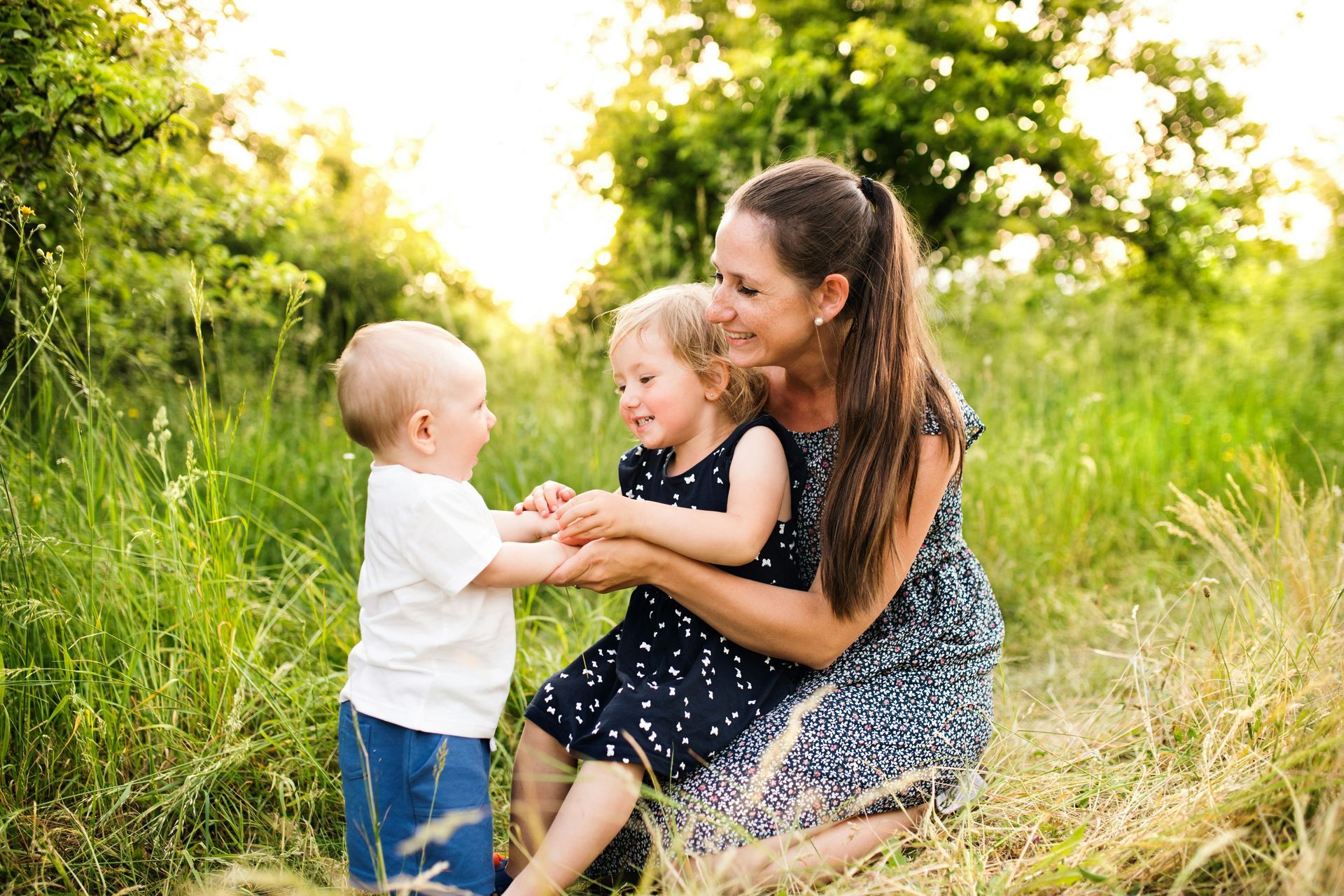 A woman is kneeling down in the grass with two children.