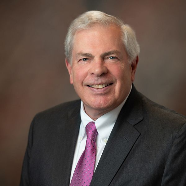 Man in suit and tie, smiling, indoors with brown background.