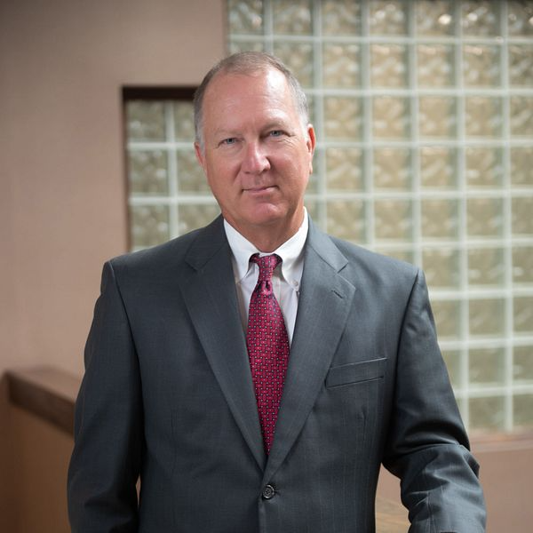 Man in gray suit and red tie, standing in a building. He is looking at the camera.