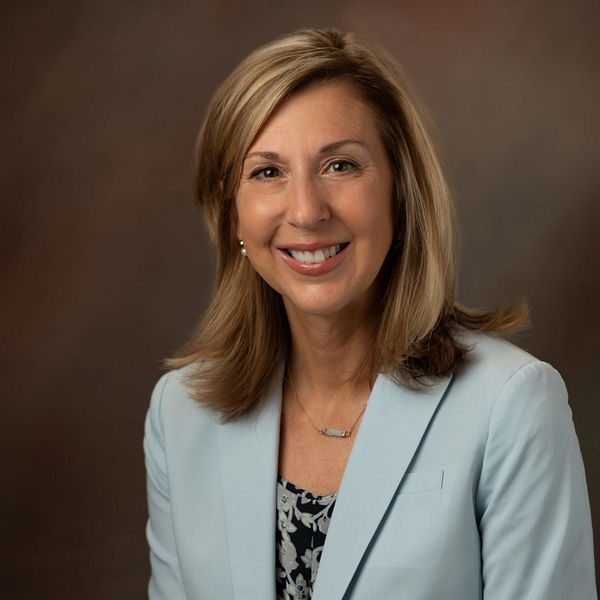 Woman in light blue blazer smiles.