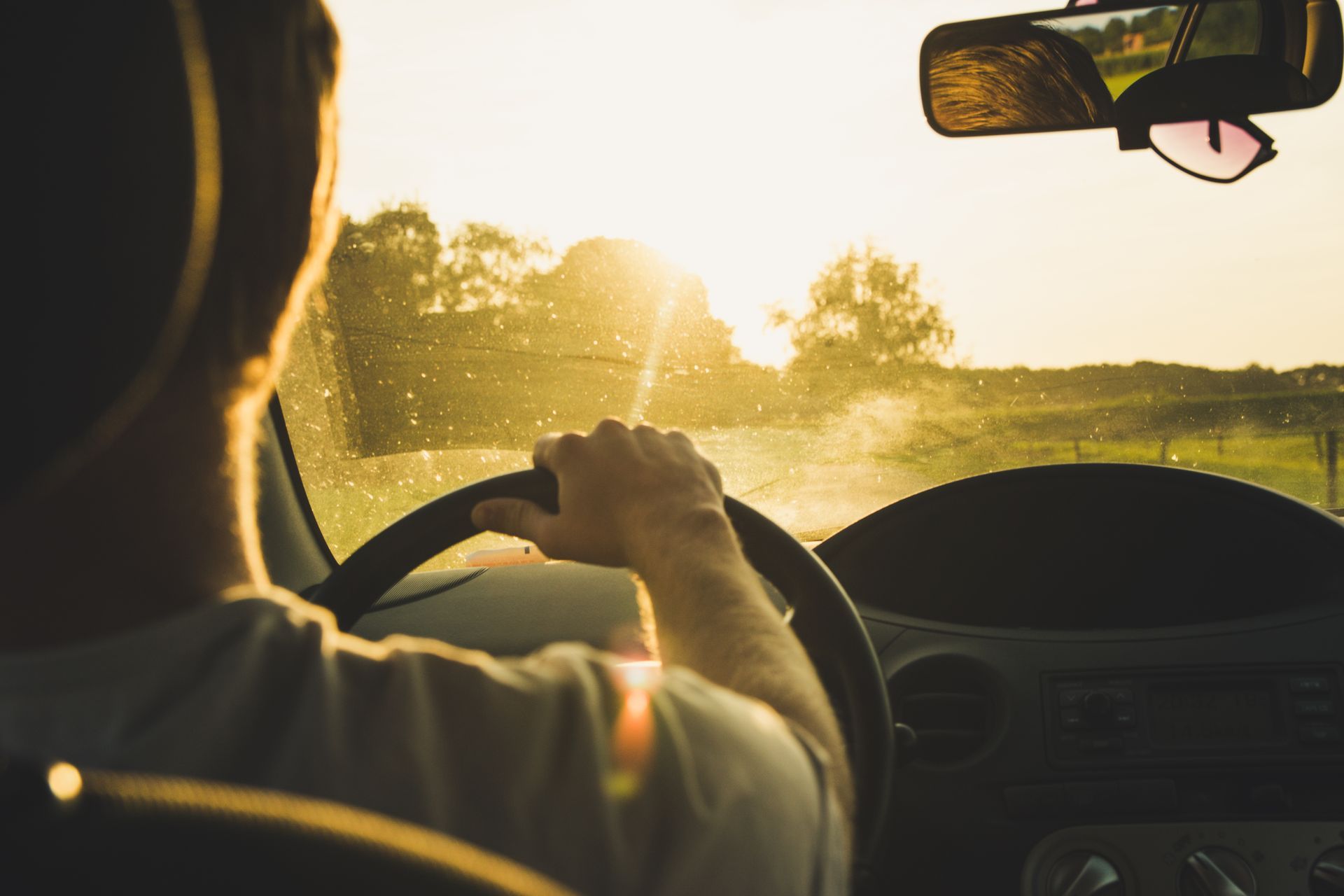 A man is driving a car on a country road at sunset.