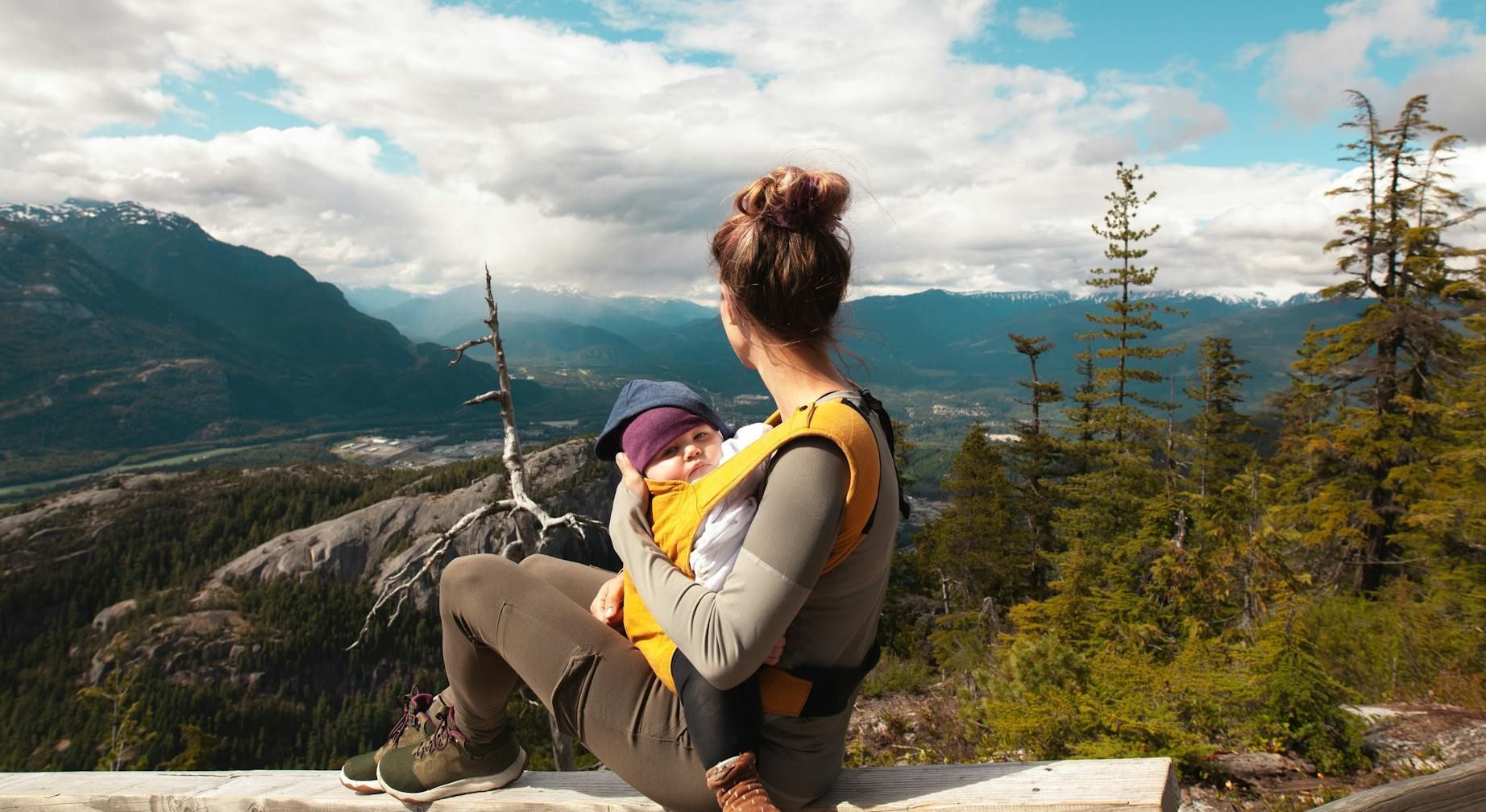 A woman is holding a baby in a carrier on top of a mountain.