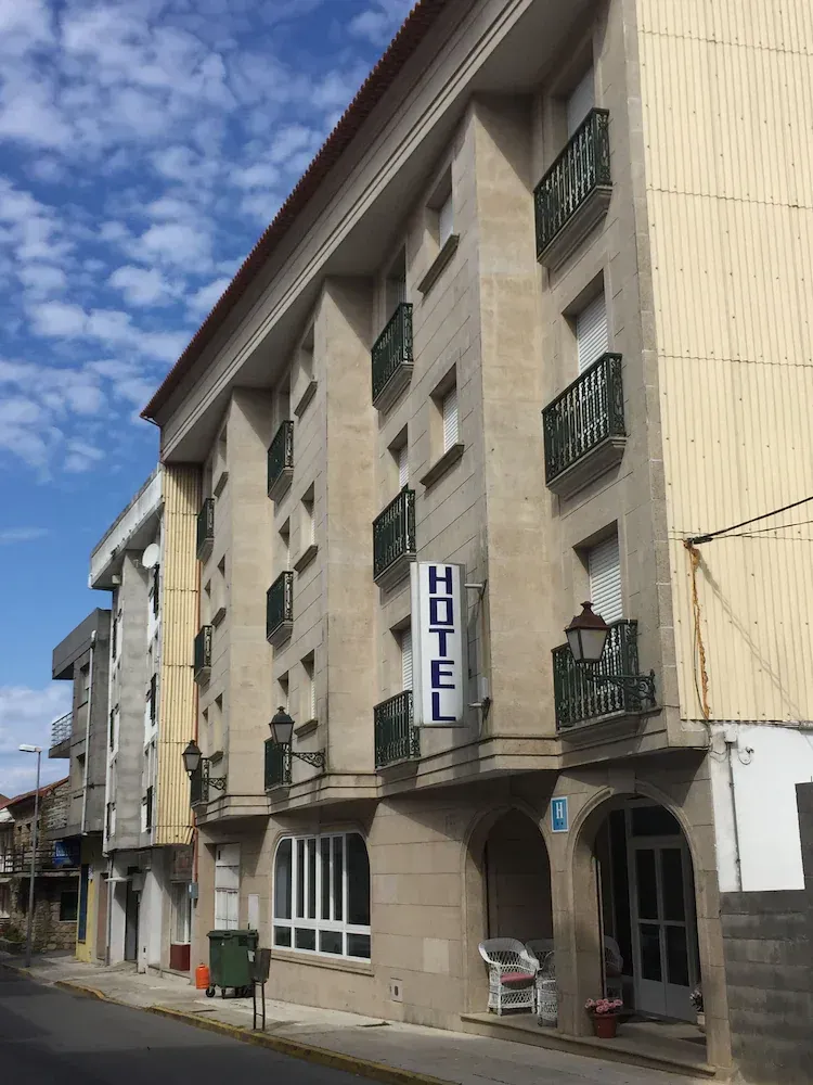 A tan stone hotel building with multiple balconies and a prominent vertical sign reading 